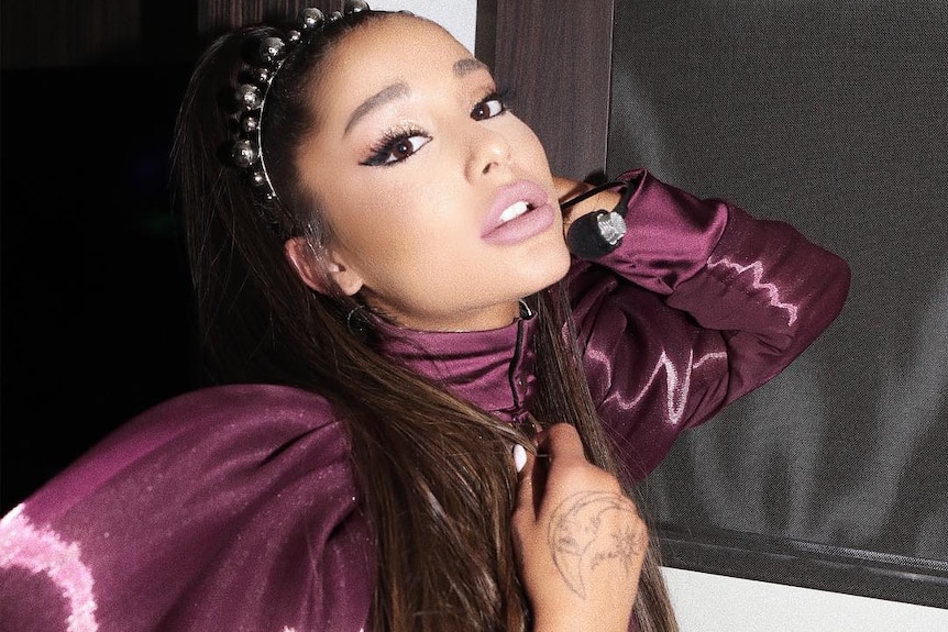 Ariana Grande wears a purple dress and does a pose.