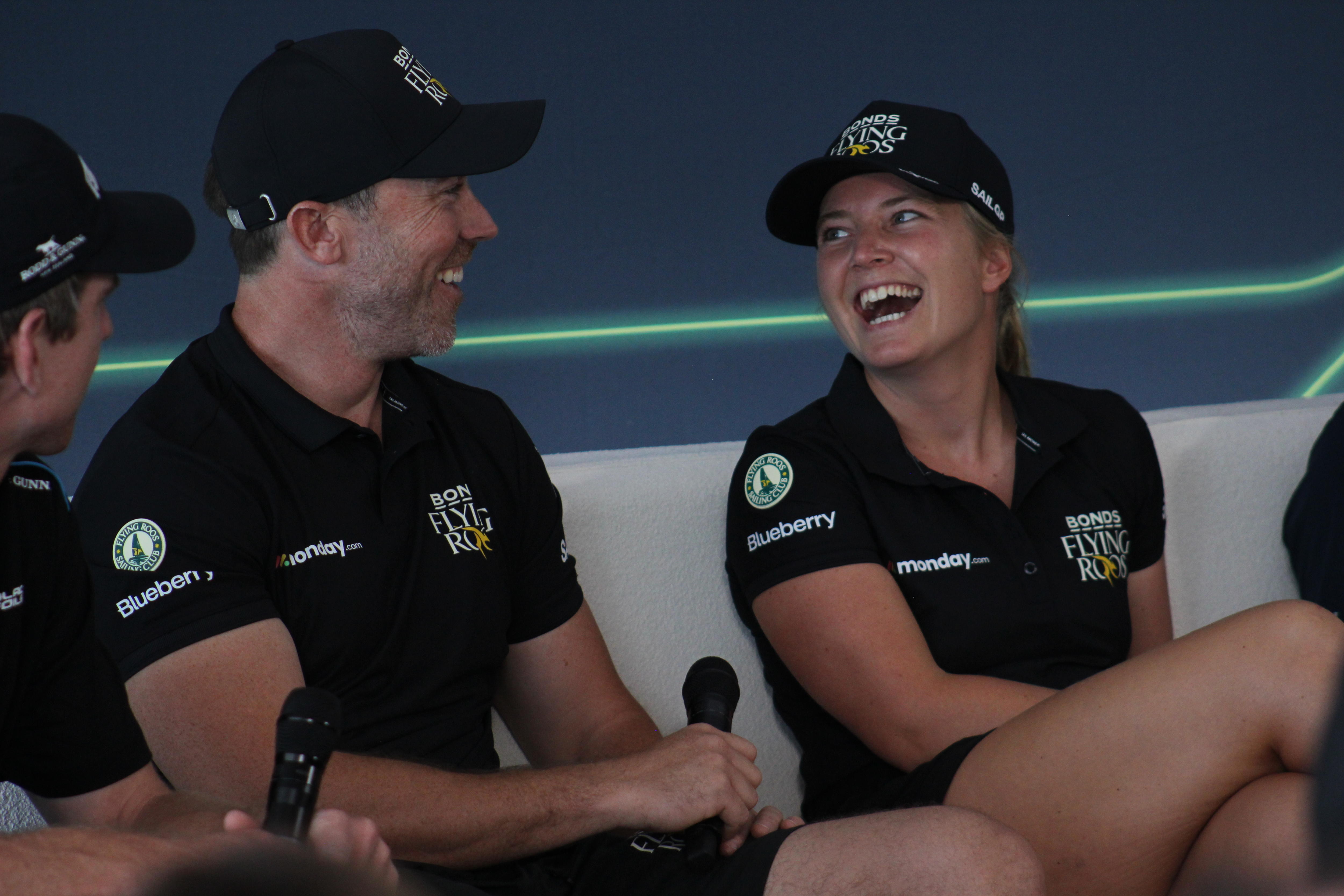 Natasha ri enquanto Kinley diz algo para ela enquanto eles se sentam um ao lado do outro.