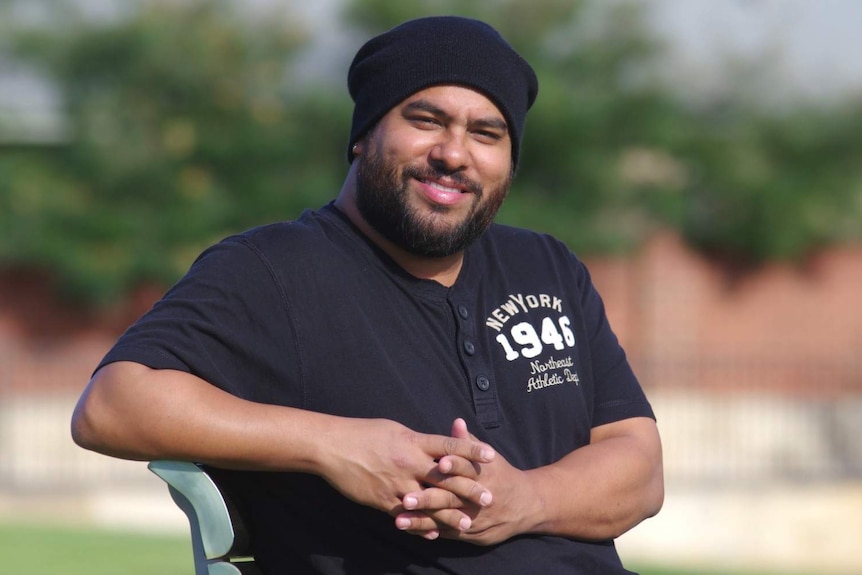 Perth musician Troy Roberts smiles and looks at the camera, sitting on a park bench.