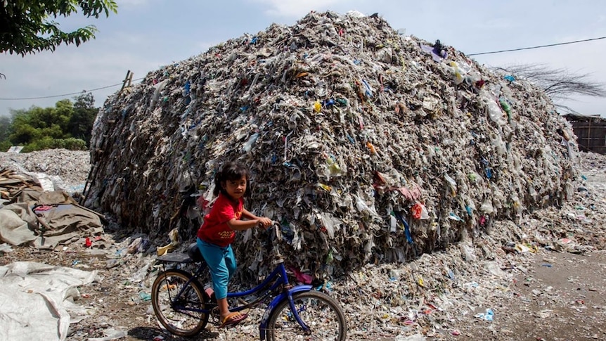 A child on a bike with a big pile of rubbish in the background.