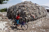 A kid on a bike with a big pile of rubbish on her background
