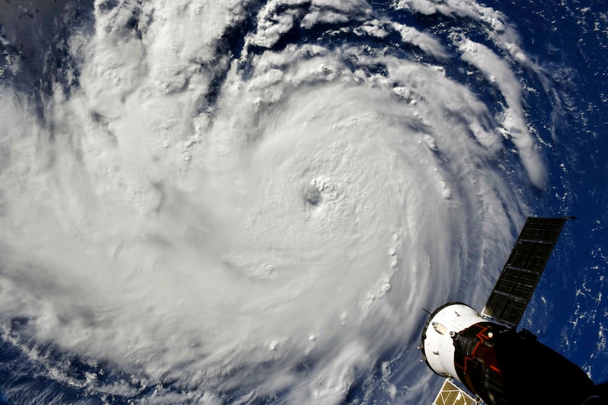 A satellite image showing a swirling mass of cloud with the International Space Station in the bottom right corner