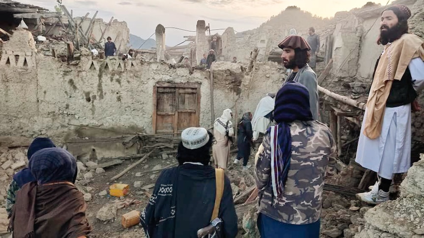 A group of Afghans look at a destroyed house caused by an earthquake