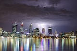 A series of bolts of lightning strike the brightly lit Perth skyline at night, with the skyline reflected in the Swan River.