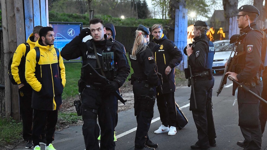 Dortmund players and police stand outside the team bus after it was hit by explosions.
