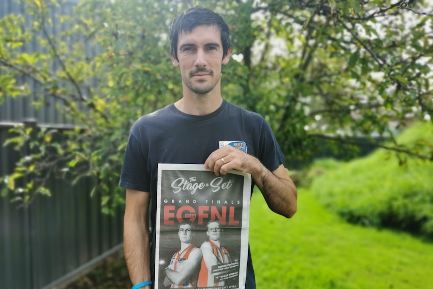 A man holds a newspaper front page up.