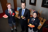 Illawarra Grammar School students Robert Martin and Meena Jasim stand with Mark Speakman, all holding fruit and vegetables.