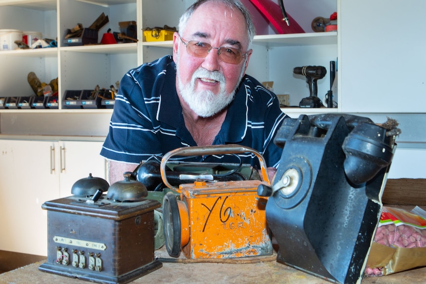 A man poses with very old phones, morse code transmitters and lamps.