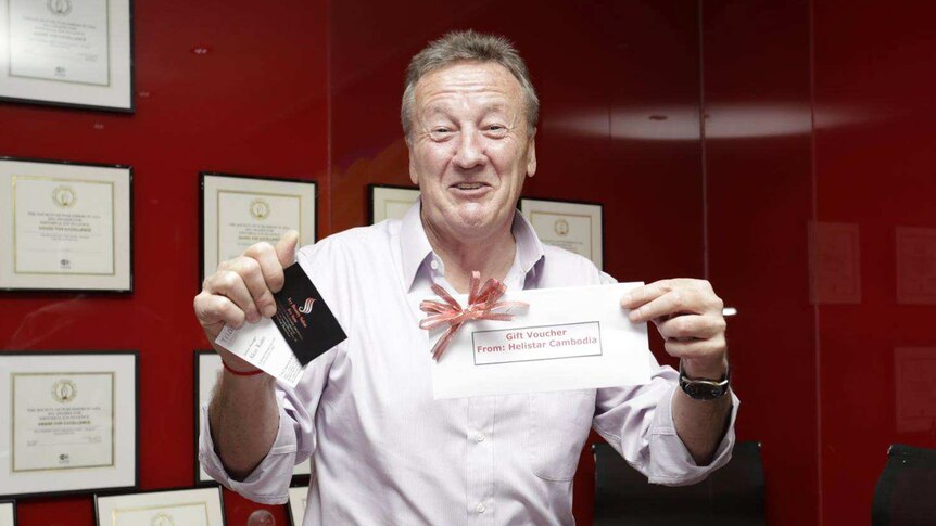 Chris Dawe smiles as he holds up a gift voucher and smiles for a photo.