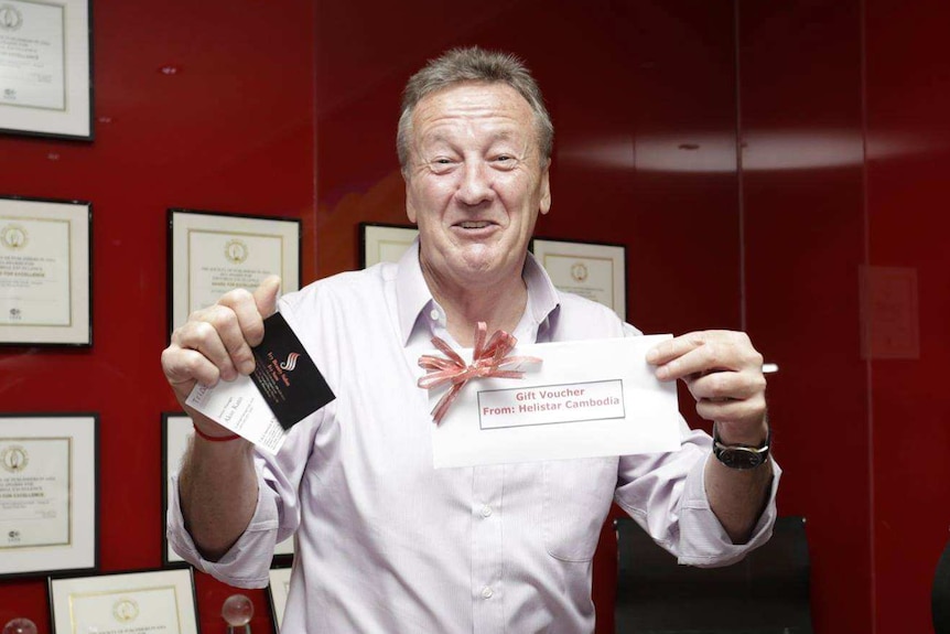 Chris Dawe smiles as he holds up a gift voucher and smiles for a photo.