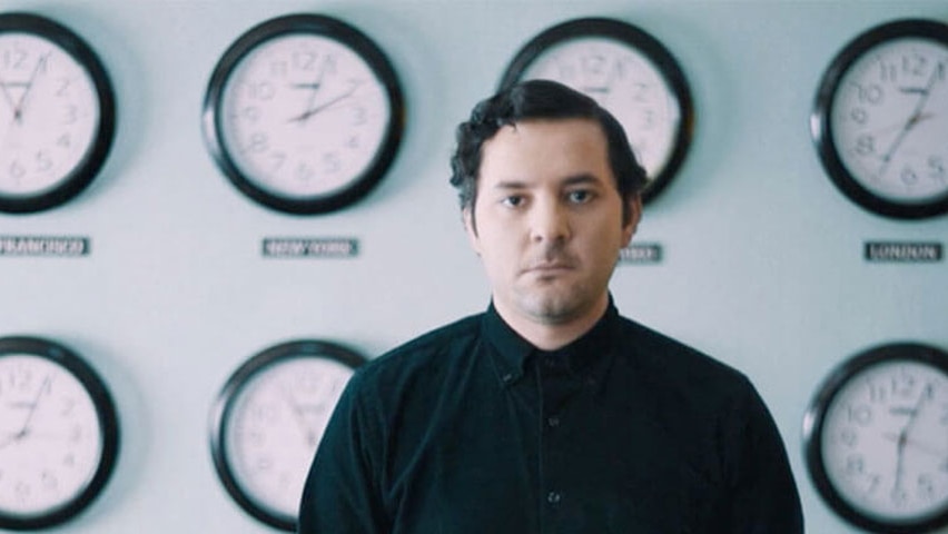 A man stand in front of a wall of clocks.