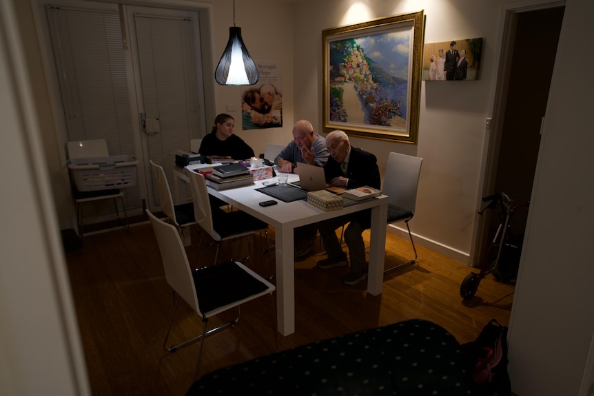 Three people it at a dining table around a computer screen