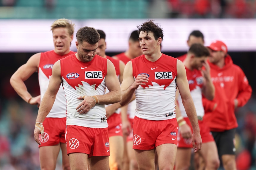 A Sydney Swans player looks at his teammates as they talk quietly on their way off the ground after a loss.