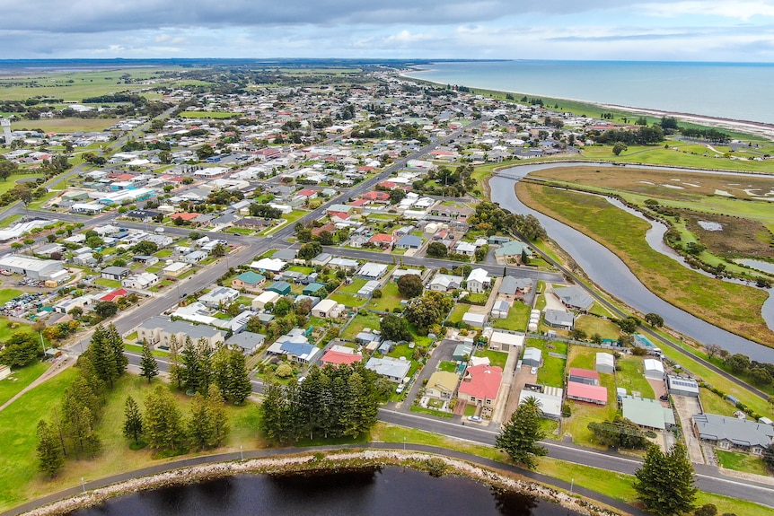 An aerial photo shows a township with large green areas and a river running towards the coastline.
