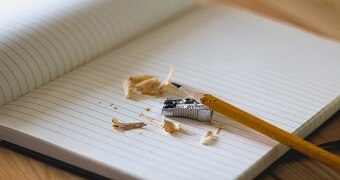 A pencil and sharpener sit on a blank notebook.
