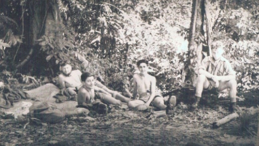 A black and white photo of four soldiers sitting on the ground and relaxing in the bush.