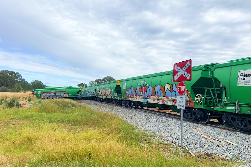 Image of graffitied freight train partially derailed near a stop sign