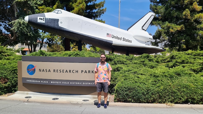 Joel Steele standing in front of a space shuttle statue at NASA headquarters. 