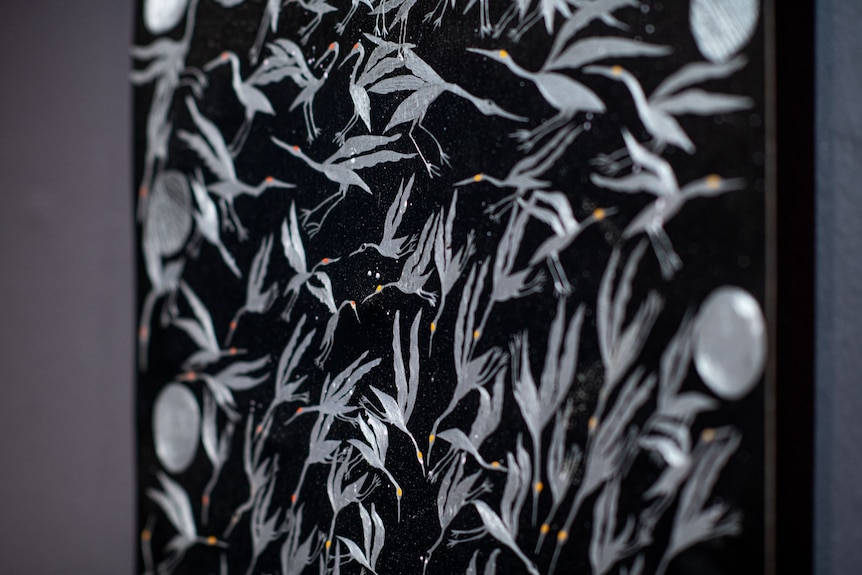 An artwork showing dozens of long necked birds etched in silver metal on a black background
