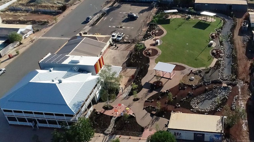 An aerial view of a two-storey building with white verandahs and an expanse of green lawn.