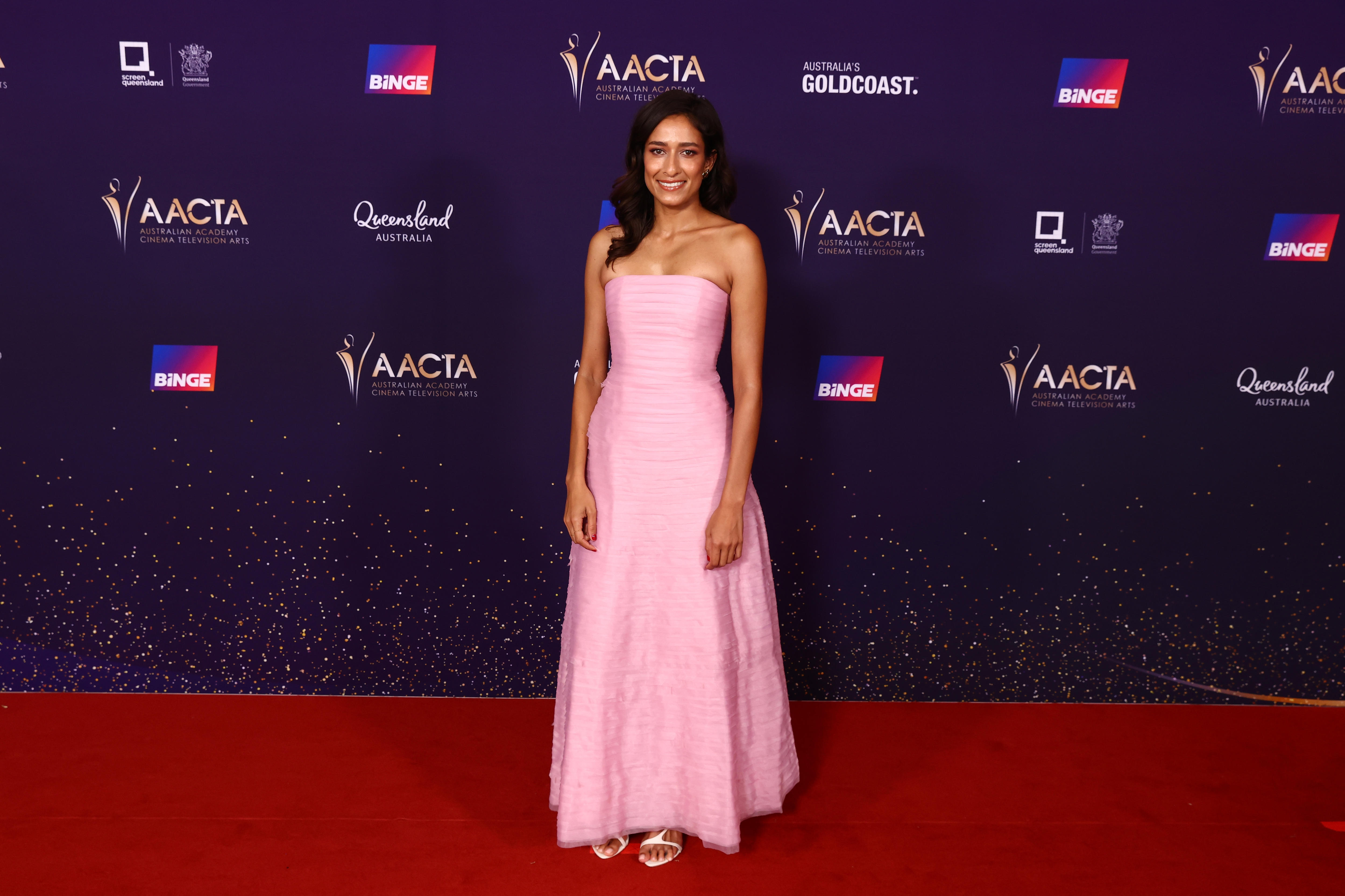 Emma Harvie wears a long, pink sleeveless dress and white sandal heels with her hair down