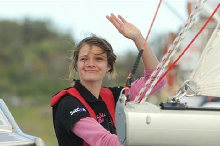 Woman standing on deck of sailing yacht wearing life jacket and waving. 