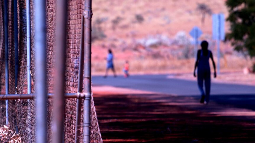 A youth walks down a street in Roebourne alongside a metal fence.