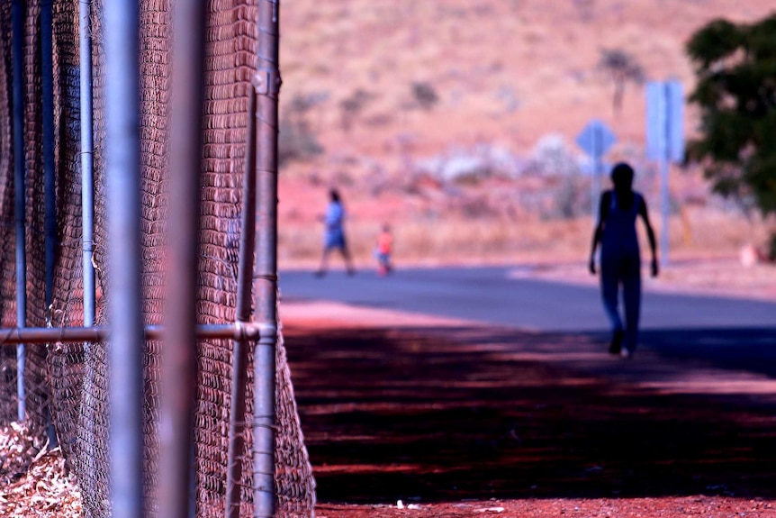 A youth walks down a street in Roebourne alongside a metal fence.