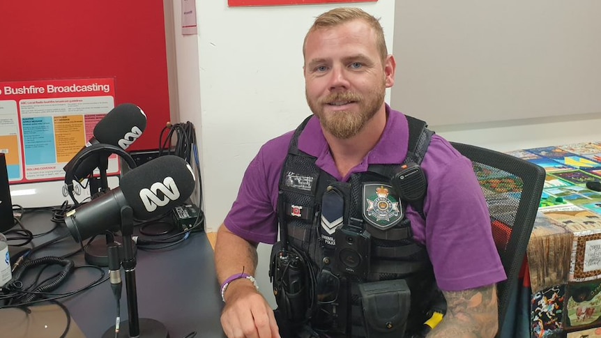 A man in a purple shirt and police vest sits in a radio studio. 