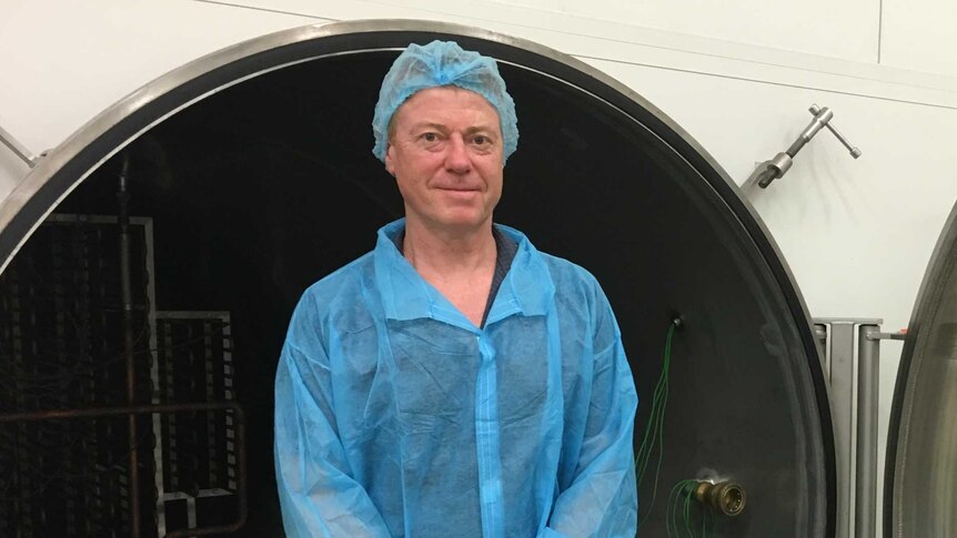 Michael Buckley stands in front of large circular dryer door dressed in hospital-style scrubs.