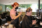 A hairdresser wears a mask while brushing a woman's hair.