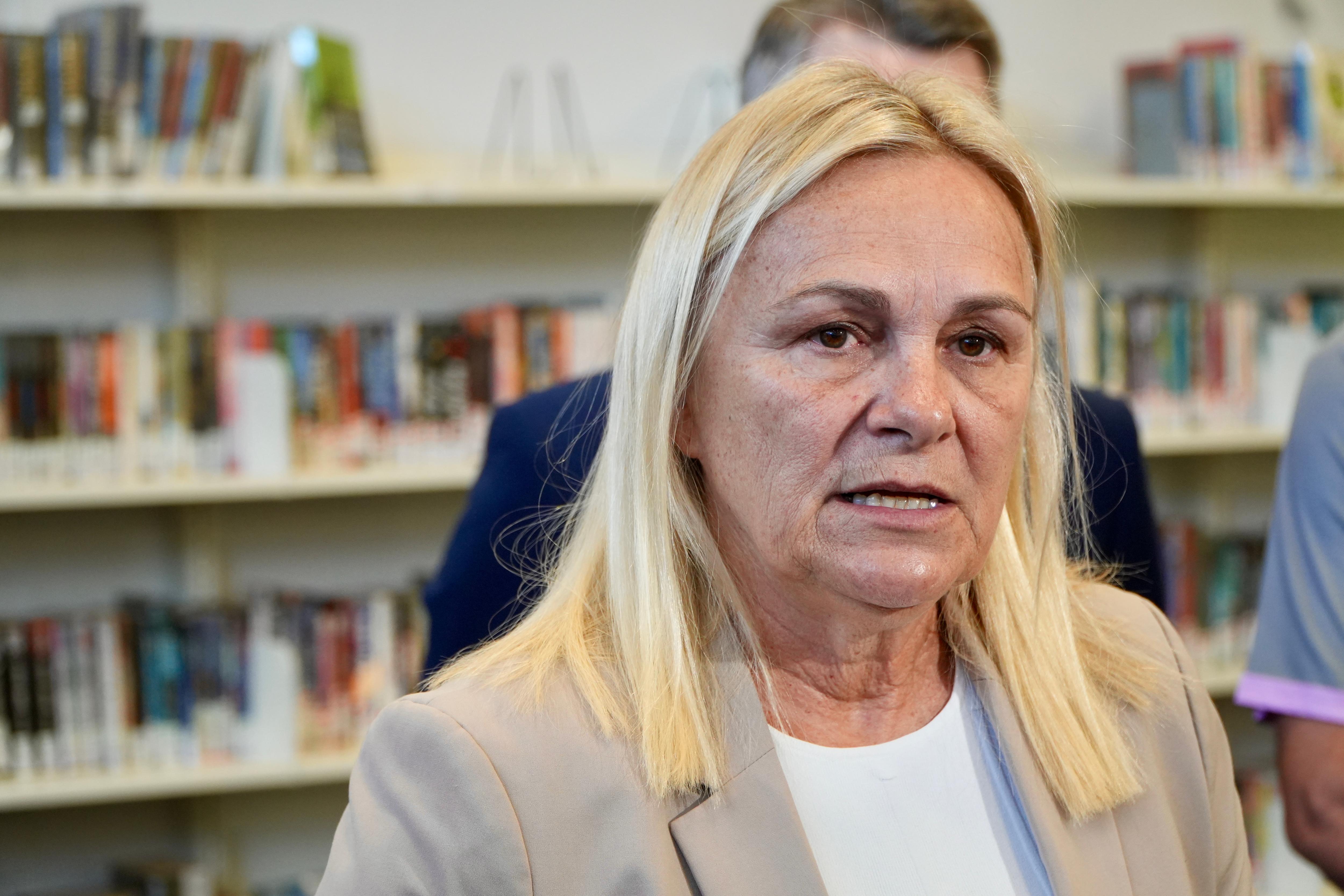 Sabine Winton usa paletó e fala para a mídia em uma biblioteca.