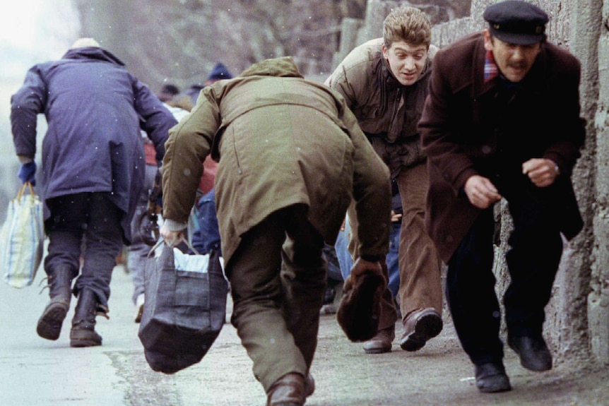 A group of people in winter coats run while ducking for cover on a street.