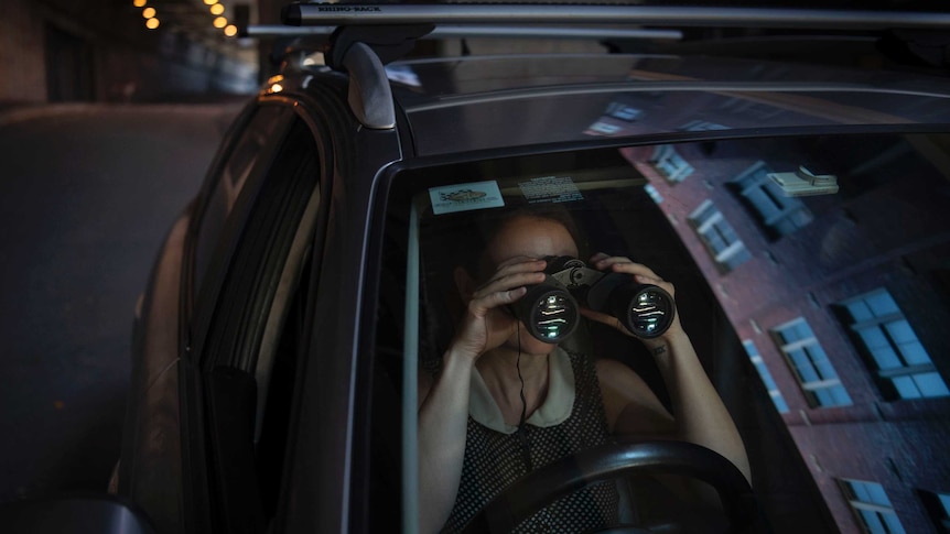 A woman sits in a car with binoculars