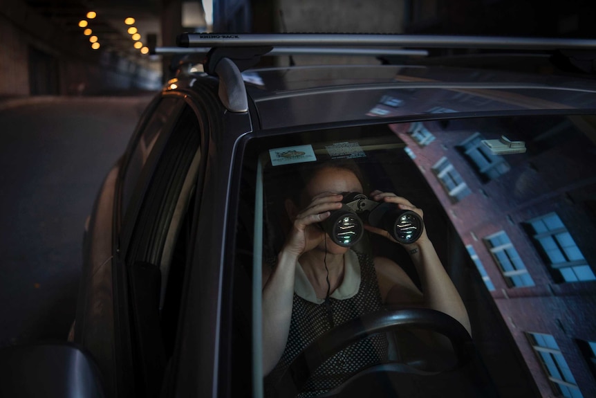 A woman sits in a car with binoculars