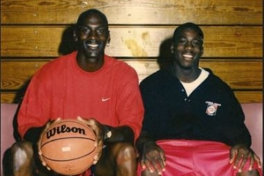 Two african-american men sit smiling on a bench, holding a basketball