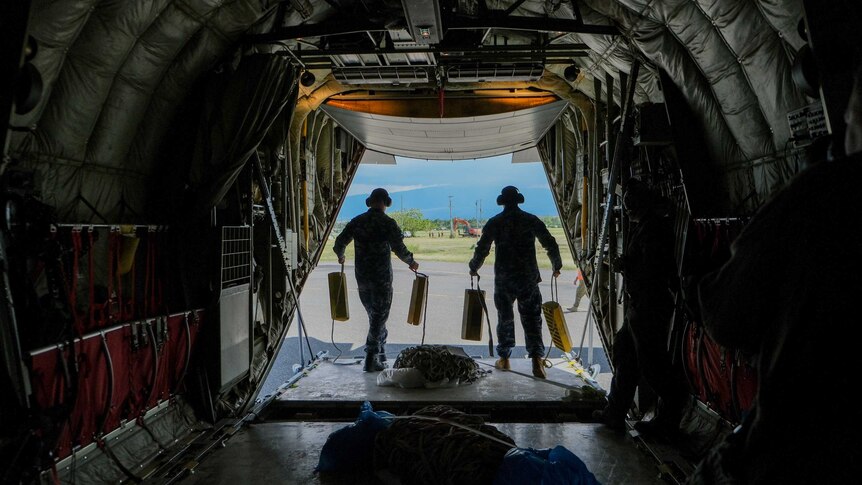 A shot from inside the aircraft with military personnel silhouetted against the a green outlook.