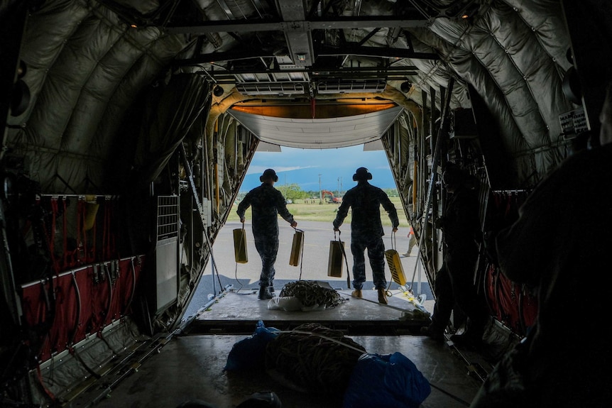 A shot from inside the aircraft with military personnel silhouetted against the a green outlook.