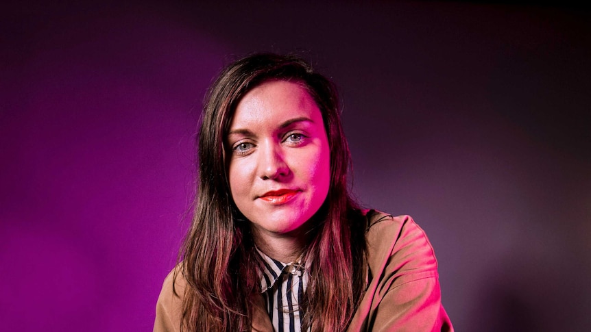 A portrait of Nat Randall, standing in front of a pink light.