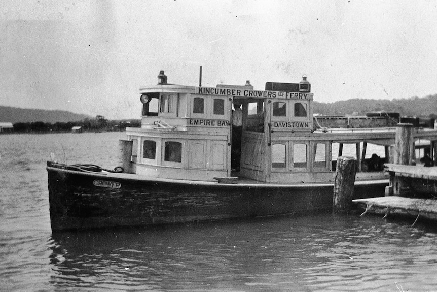 A black and white photo of a ferry on water with 'kincumber growers ltd ferry' on the side