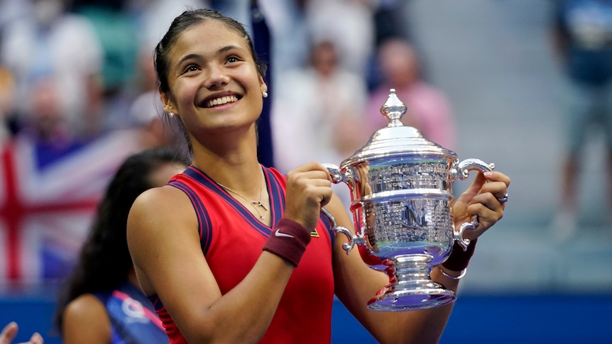 Britain's Emma Raducanu has a beaming smile as she holds the US Open trophy with both hands.