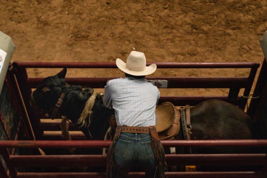 a man in a cowboy hat prepares to mount a horse.