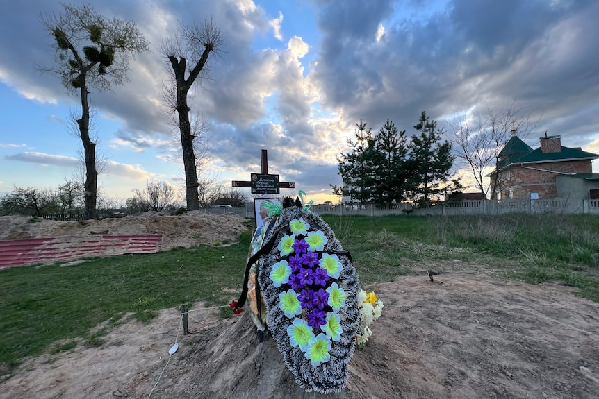 A floral garland sits on top of a grave in a field near a brick home. 