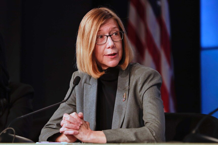 A woman with glasses on is seated with a microphone in front of her