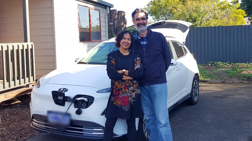 A woman and a man posing in front of their electric vehicle while it's charging.