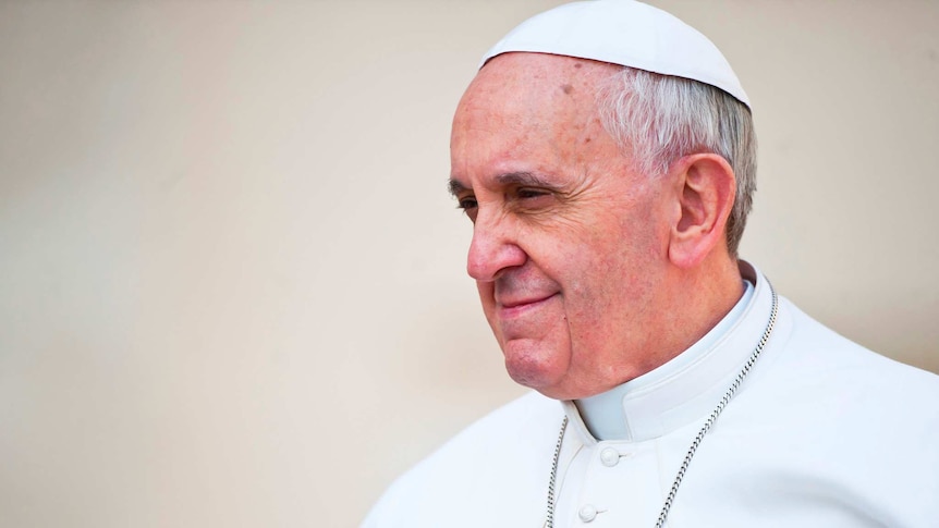 Pope Francis wearing a white zucchetto and robe and silver chain, looking to his right