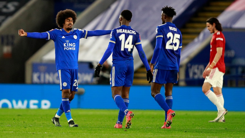 Three Leicester players wearing blue kit smile as a player wearing red looks sad in the background 