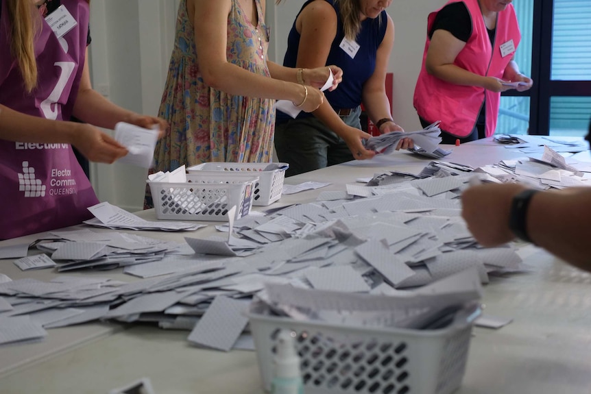 Four Electoral Commission Queensland staff count ballot papers, ballot papers scattered all over table.