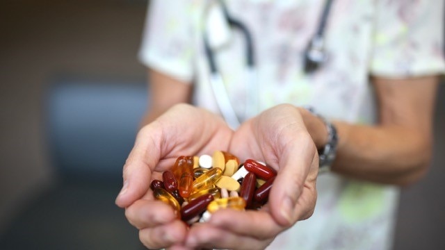 An unidentified doctor holds a pile of red, yellow and white complementary medicine pills in their outstretched hands.