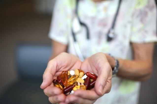 An unidentified doctor holds a pile of red, yellow and white complementary medicine pills in their outstretched hands.